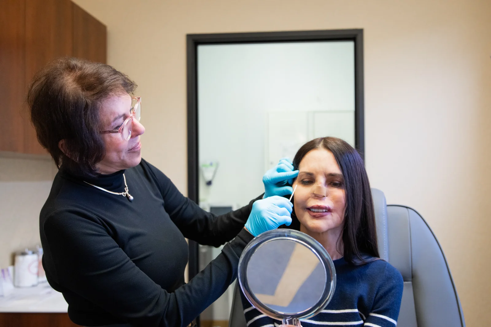 Dr. Gayle Misle performing an injectable treatment while the patient follows in a hand mirror at Reviv Med Spa, Millbrae